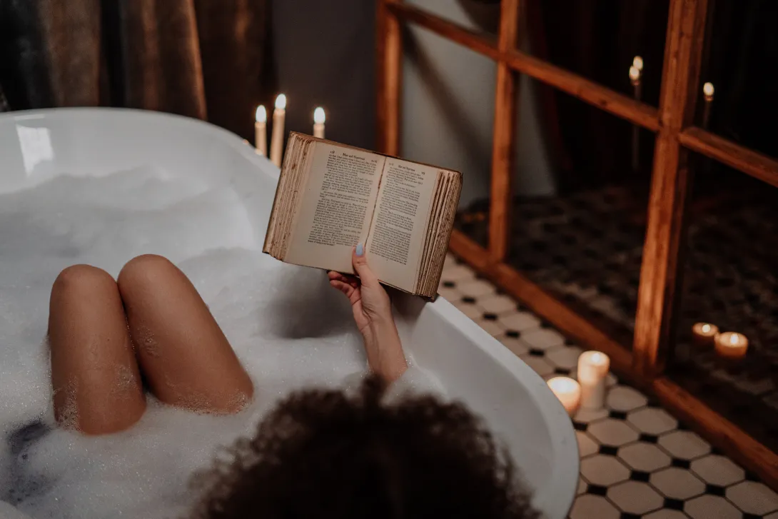 Brown person reading a book in a relaxing bath soak
